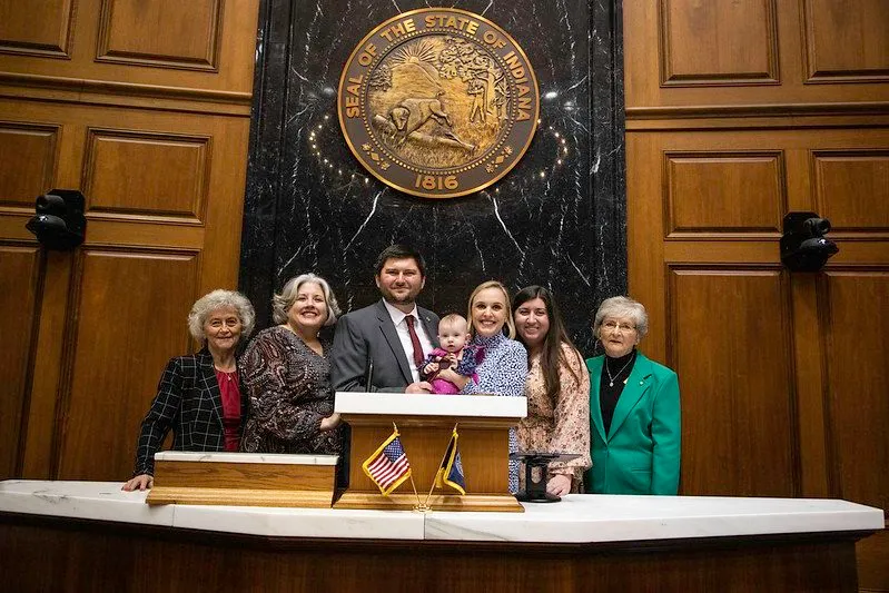 Kyle Pierce with his wife, baby daughter, and family at the Speaker's rostrum beneath the Indiana state seal